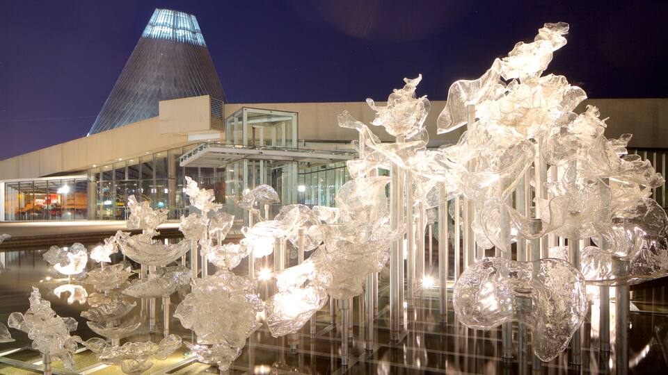A modern building with a unique glass pyramid structure and a glass sculpture installation in front.
