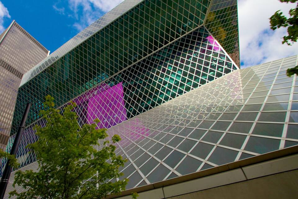 Een modern glazen gebouw met een geometrisch gevelontwerp, omgeven door andere hoge gebouwen.