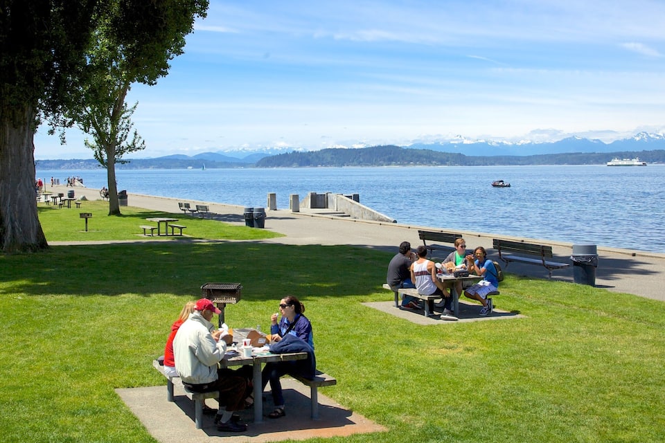 A lakeside park with picnic tables and benches, a walking path, and boats on the water.