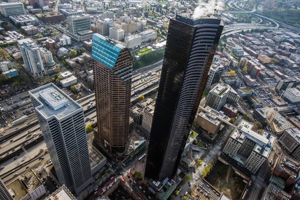 A cityscape with two prominent skyscrapers, a dense urban area, and a highway in the background.