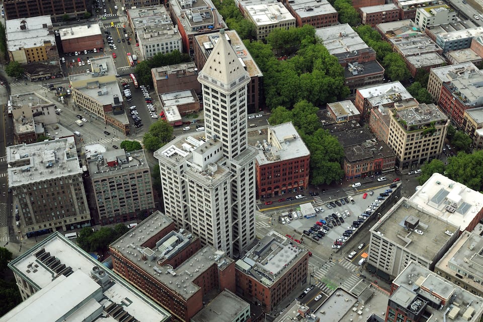 An aerial view of a cityscape with a prominent white tower, dense urban buildings, and a network of streets.