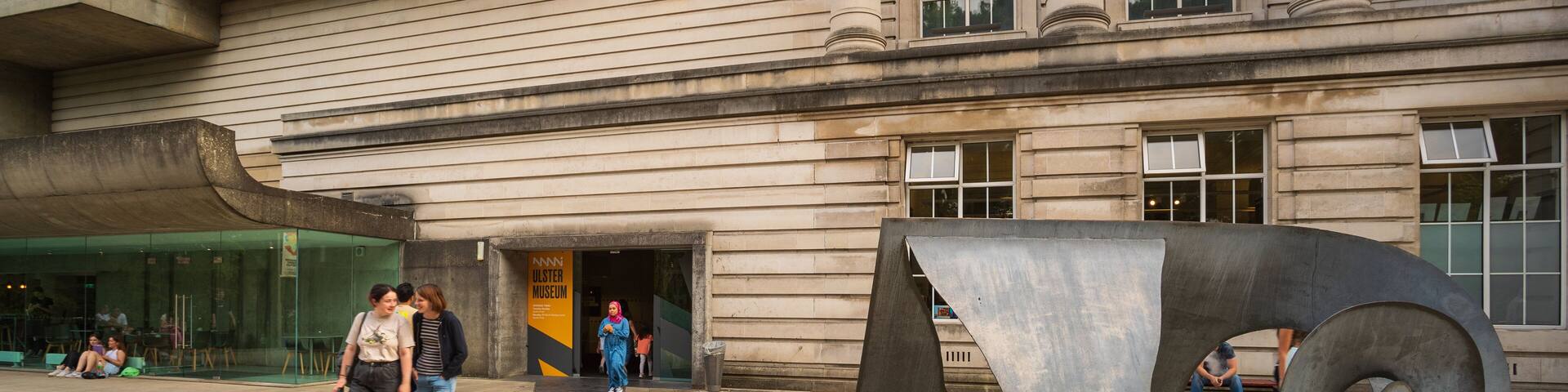 A large metal sculpture in front of a building with a sign for the Ulster Museum.