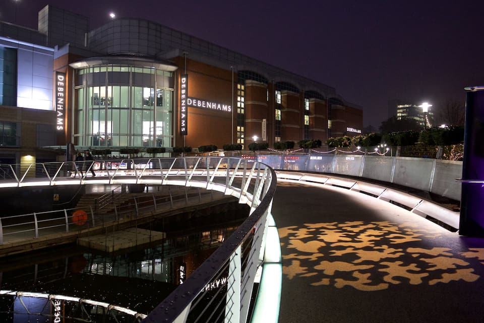A modern shopping center with a curved bridge and a large glass facade.