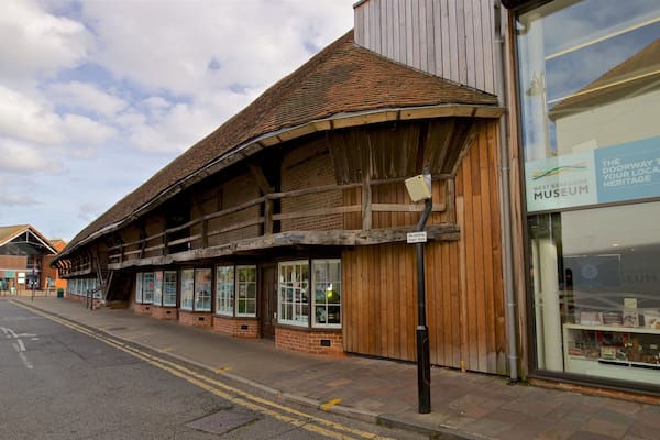 Un bâtiment traditionnel en bois auquel a été ajoutée une extension moderne en verre, une rue avec des lignes jaunes doubles au sol, et un panneau indiquant le musée du West Berkshire.