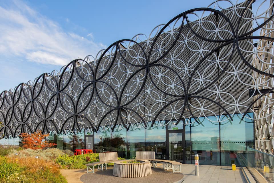 Een modern gebouw met een opvallende, geometrische metalen gevel en een terras.
