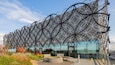 Un edificio moderno con una facciata in metallo dalla geometria originale e un'area salotto all'aperto.