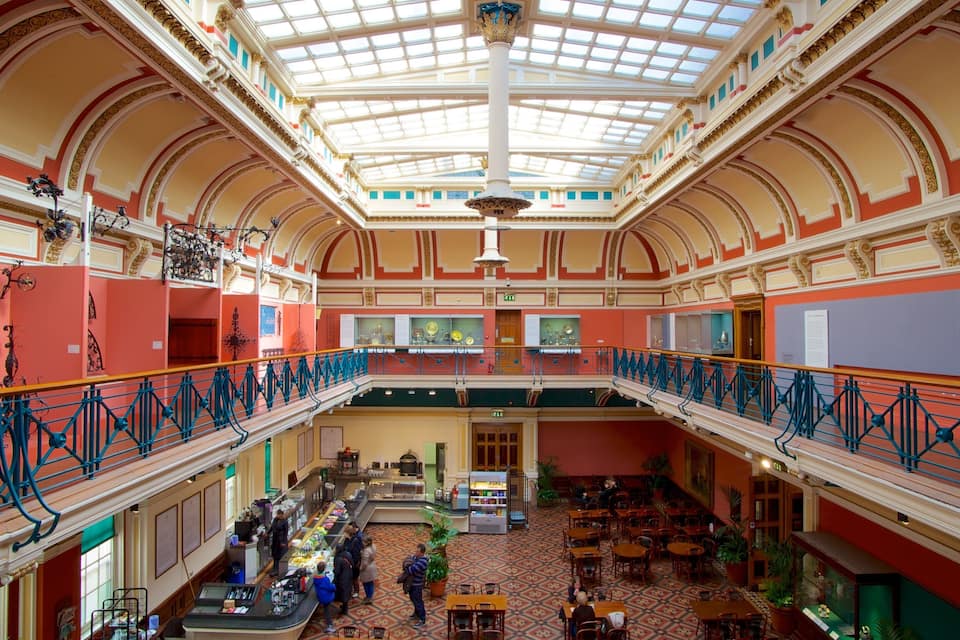 A grand, ornately decorated hall with a high ceiling, a central staircase, and a lower level with tables and chairs.