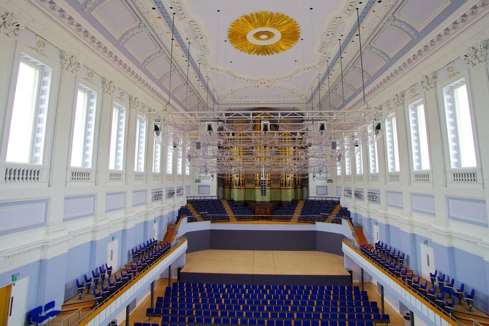 An auditorium with blue seats, a stage, and ornate ceiling decorations.