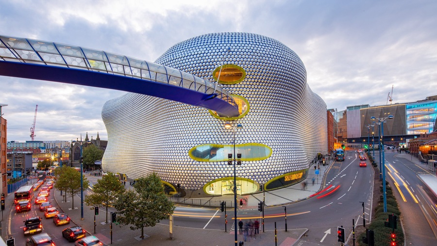A modern spherical building with a reflective surface, surrounded by a busy urban street with traffic lights and a pedestrian overpass.