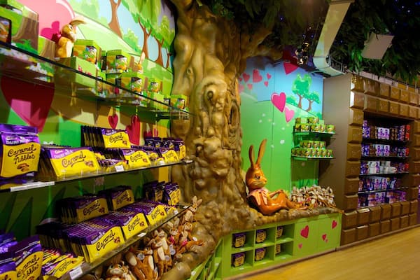 A candy store with shelves of caramel and chocolate bars, a large tree sculpture, and a rabbit statue.