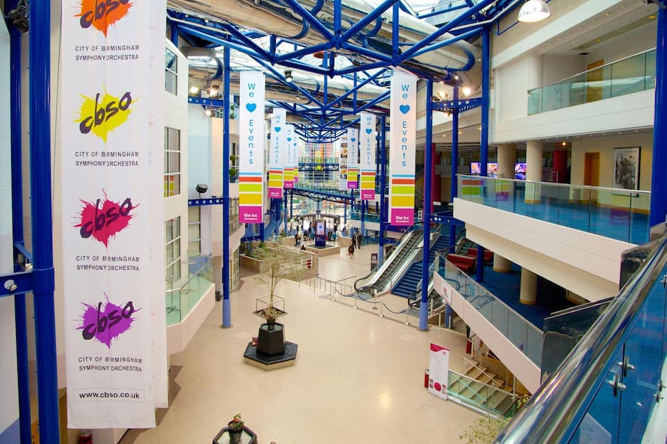 A modern indoor atrium with blue structural beams, multiple levels, and banners for the City of Birmingham Symphony Orchestra.