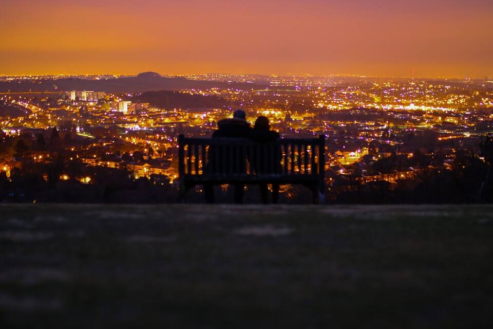 A bench overlooking a cityscape at dusk with lights illuminating the buildings.