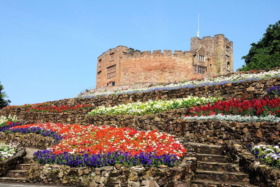 A castle atop a stone wall with colorful flower arrangements.