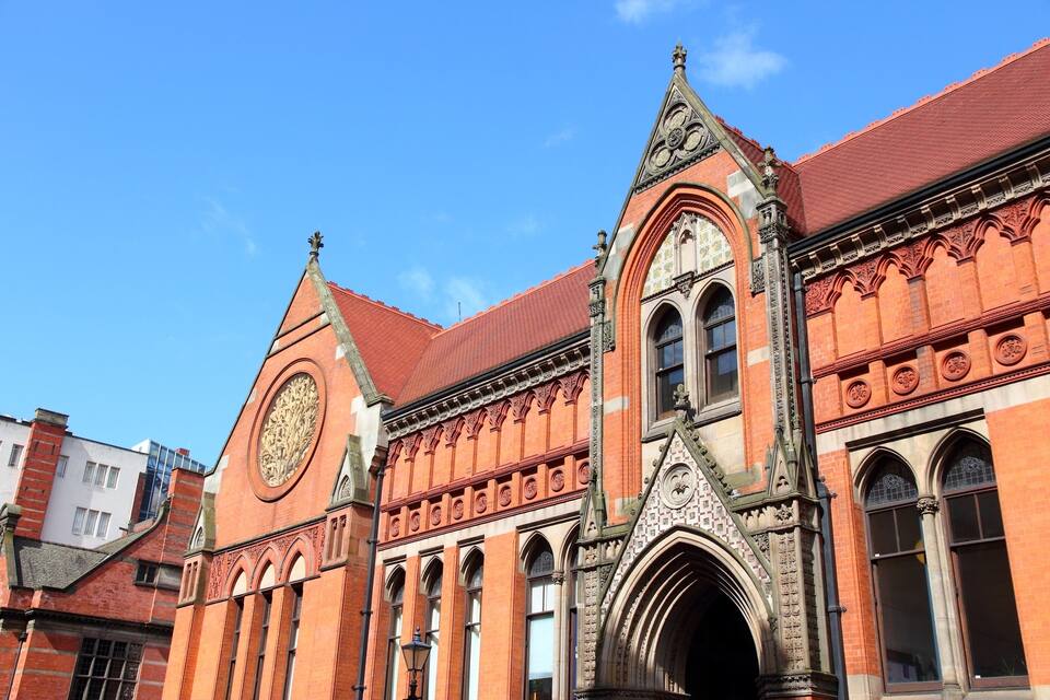 A historic building with intricate brickwork, pointed arches, and a prominent clock tower.