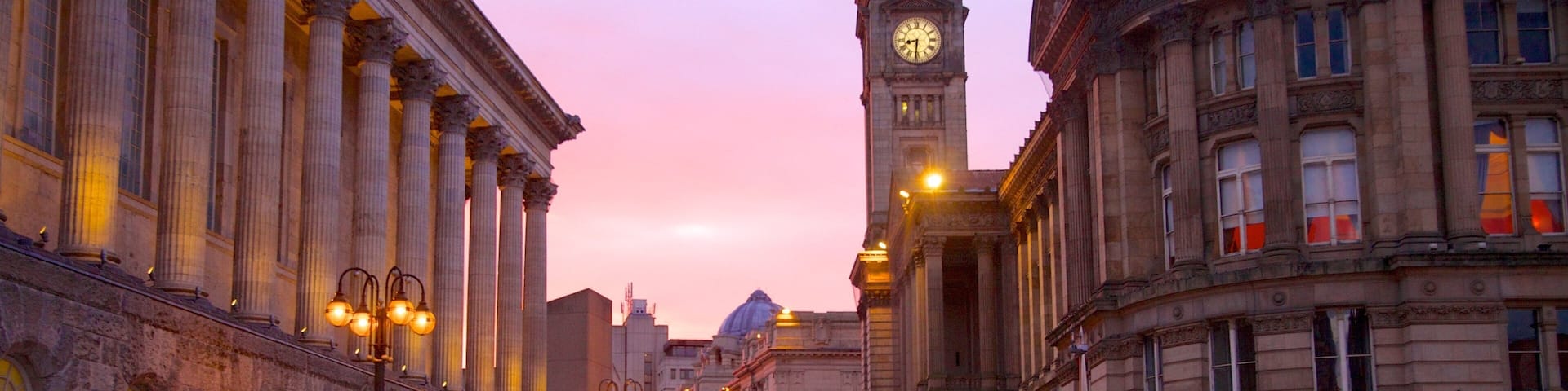 A historic street with classical architecture, a prominent clock tower, and illuminated street lamps.