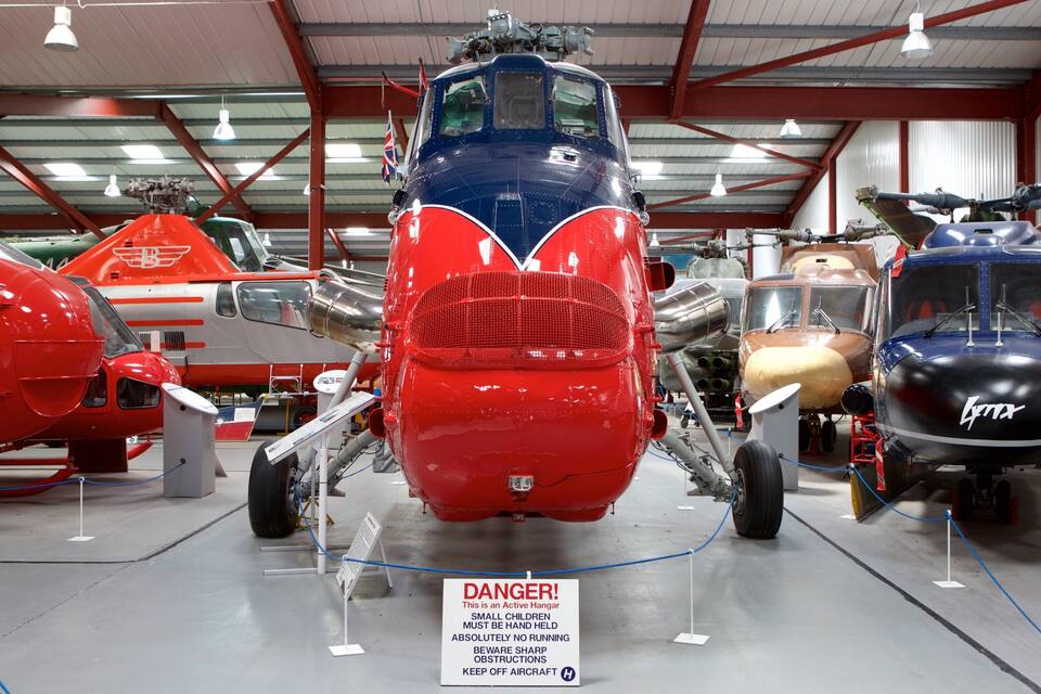 A hangar with various aircraft on display, including a red and blue helicopter in the foreground.