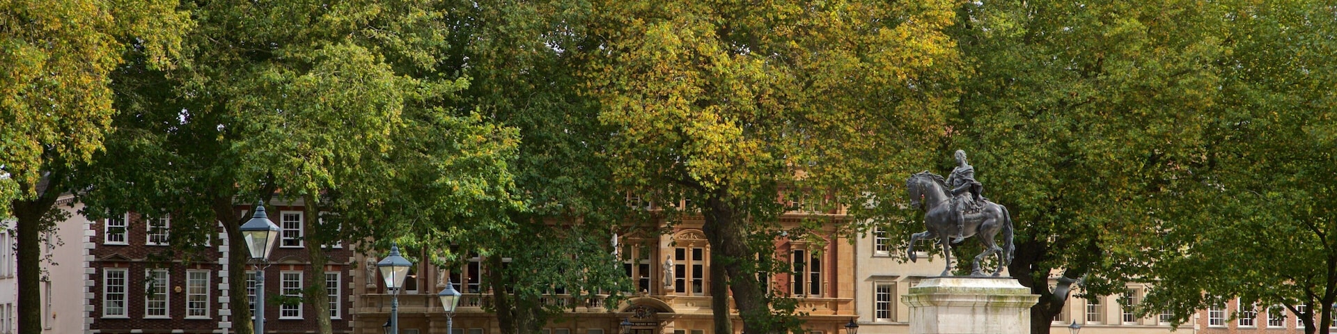 Queen Square featuring a statue or sculpture and a garden as well as a small group of people