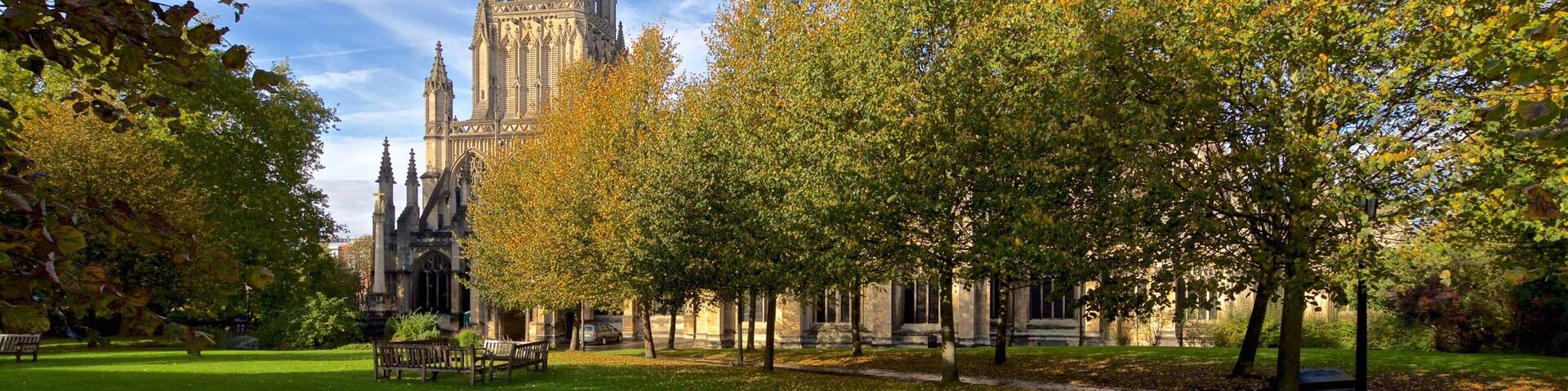 A cathedral with a tall spire, surrounded by autumn trees and a grassy park area.