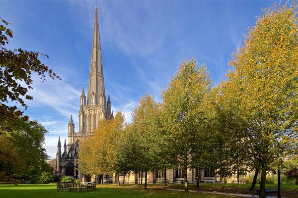 Une cathédrale dotée d’un flèche imposante, entourée d’arbres aux couleurs automnales et d’un espace vert aménagé en parc.