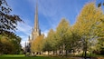 A cathedral with a tall spire, surrounded by autumn trees and a grassy park area.