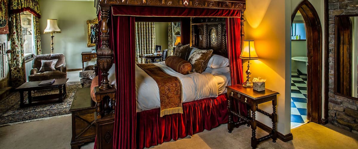 A four-poster bed with red drapery, a chandelier, and a stone wall.