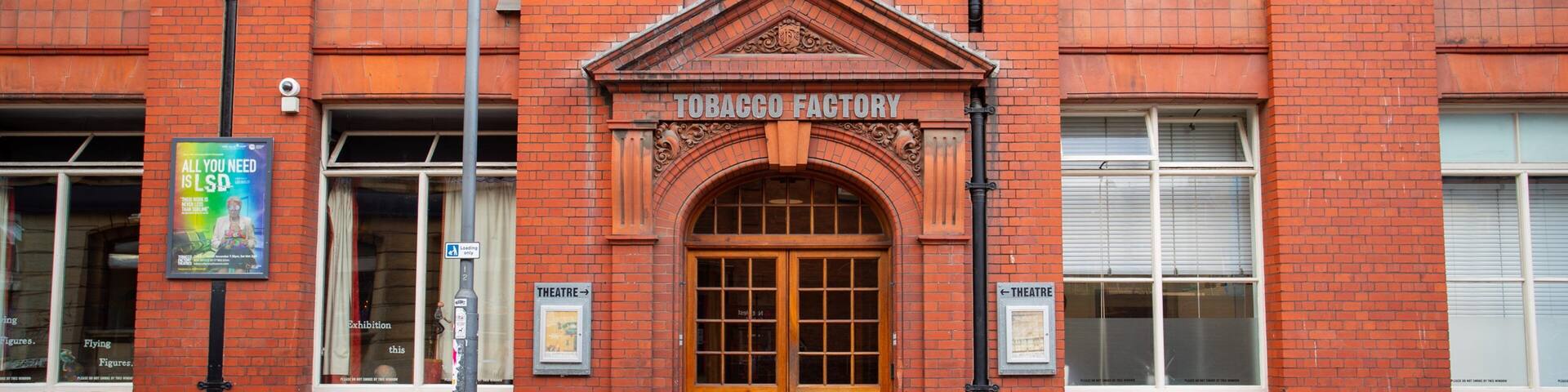 A red brick building with a wooden double door and a sign that reads "TOBACCO FACTORY".