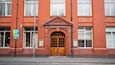 Un bâtiment en briques rouges, doté d’une double porte en bois et d’une enseigne indiquant « FABRIQUE DE TABAC ».