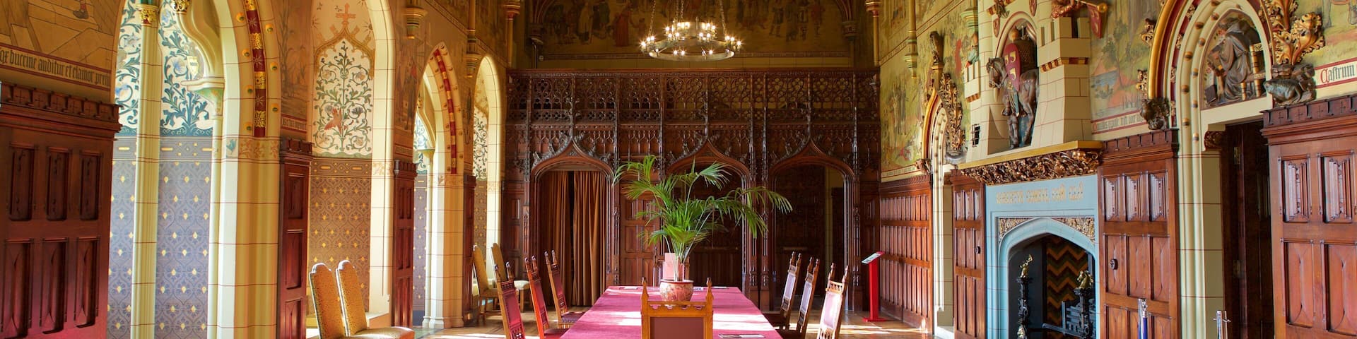 An ornate hall with high wooden ceilings, intricate murals, and a central table with a red cloth.