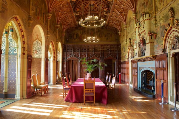 An ornate hall with high wooden ceilings, intricate murals, and a central table with a red cloth.