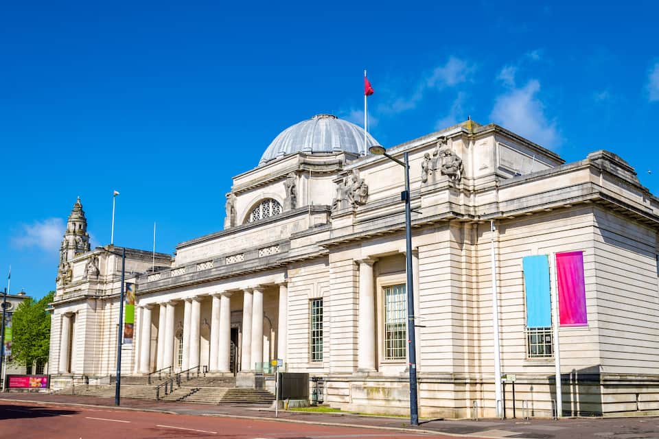 Un edificio clásico con una gran cúpula y columnas, una bandera y una escalera que conduce a la entrada.