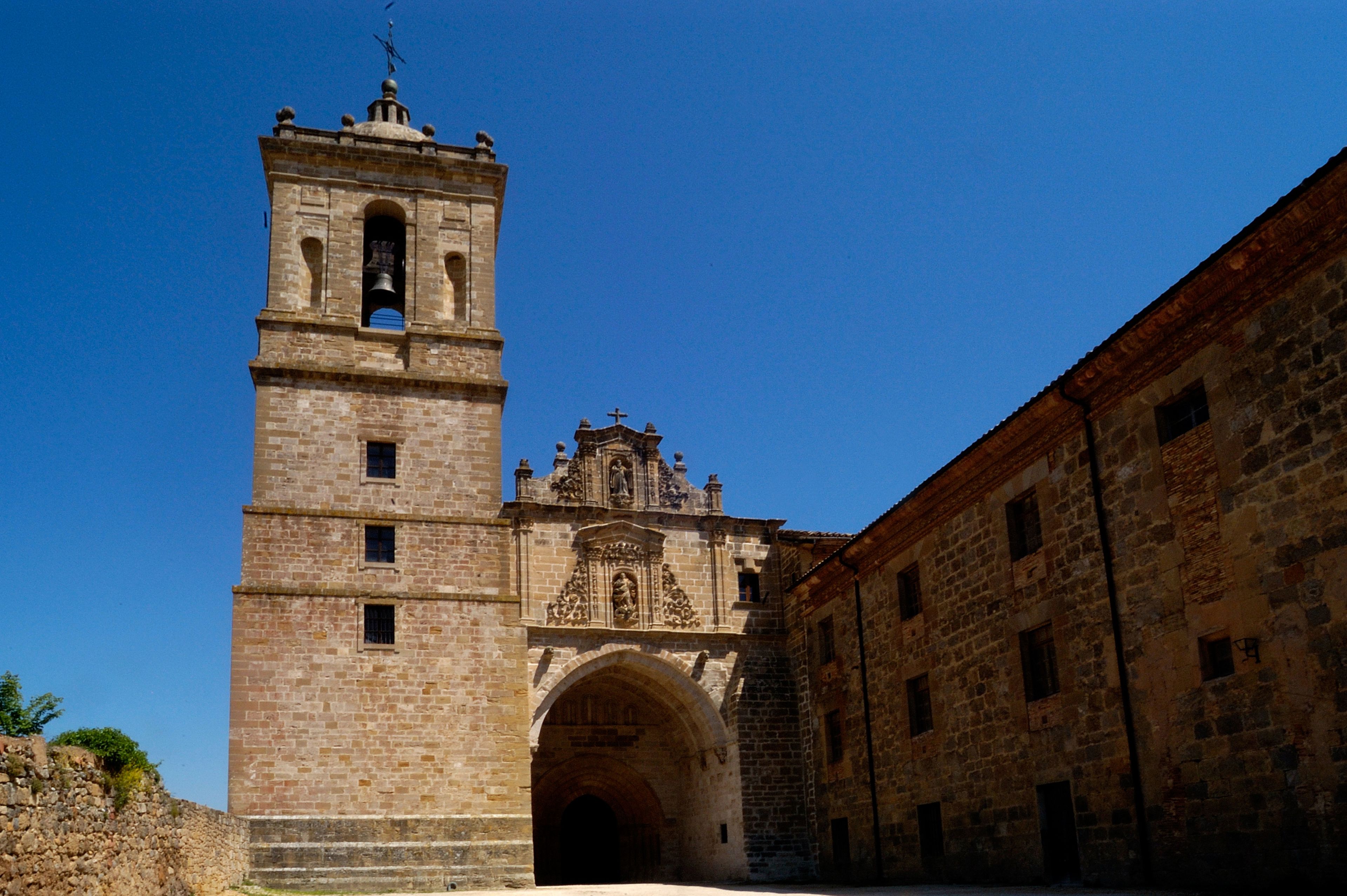 A historic stone tower with a bell, an ornate doorway, and a clear blue sky.