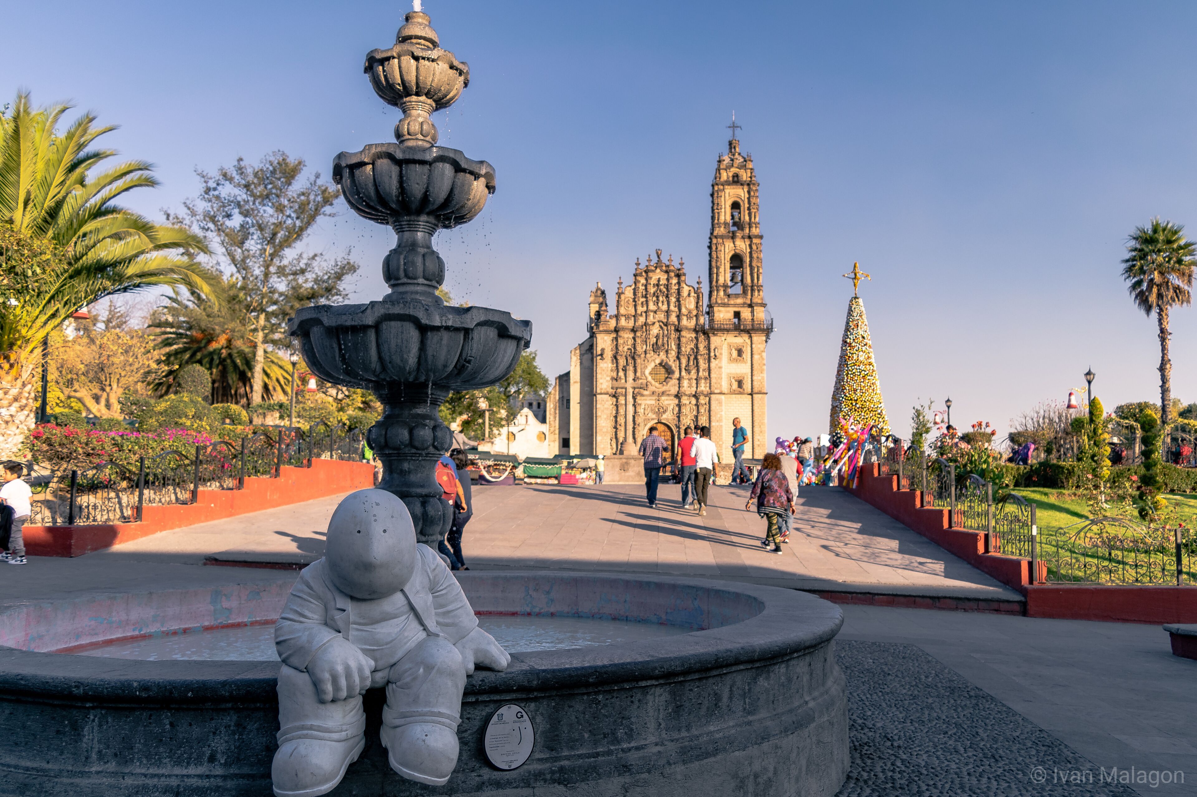 Una fuente, una estatua blanca de grandes dimensiones e iglesia histórica con un campanario.
