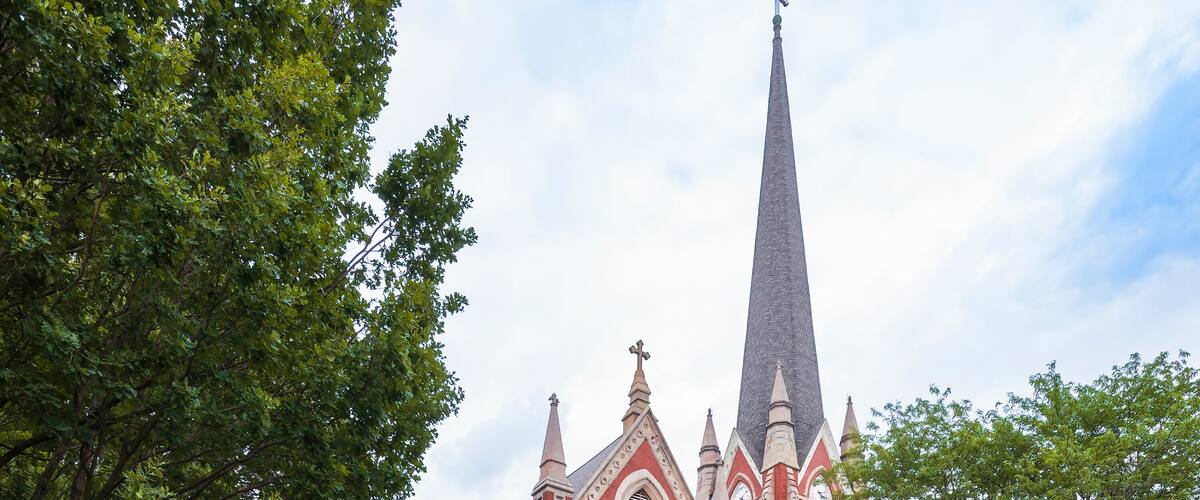 A large red brick church with a tall steeple and Gothic architecture.
