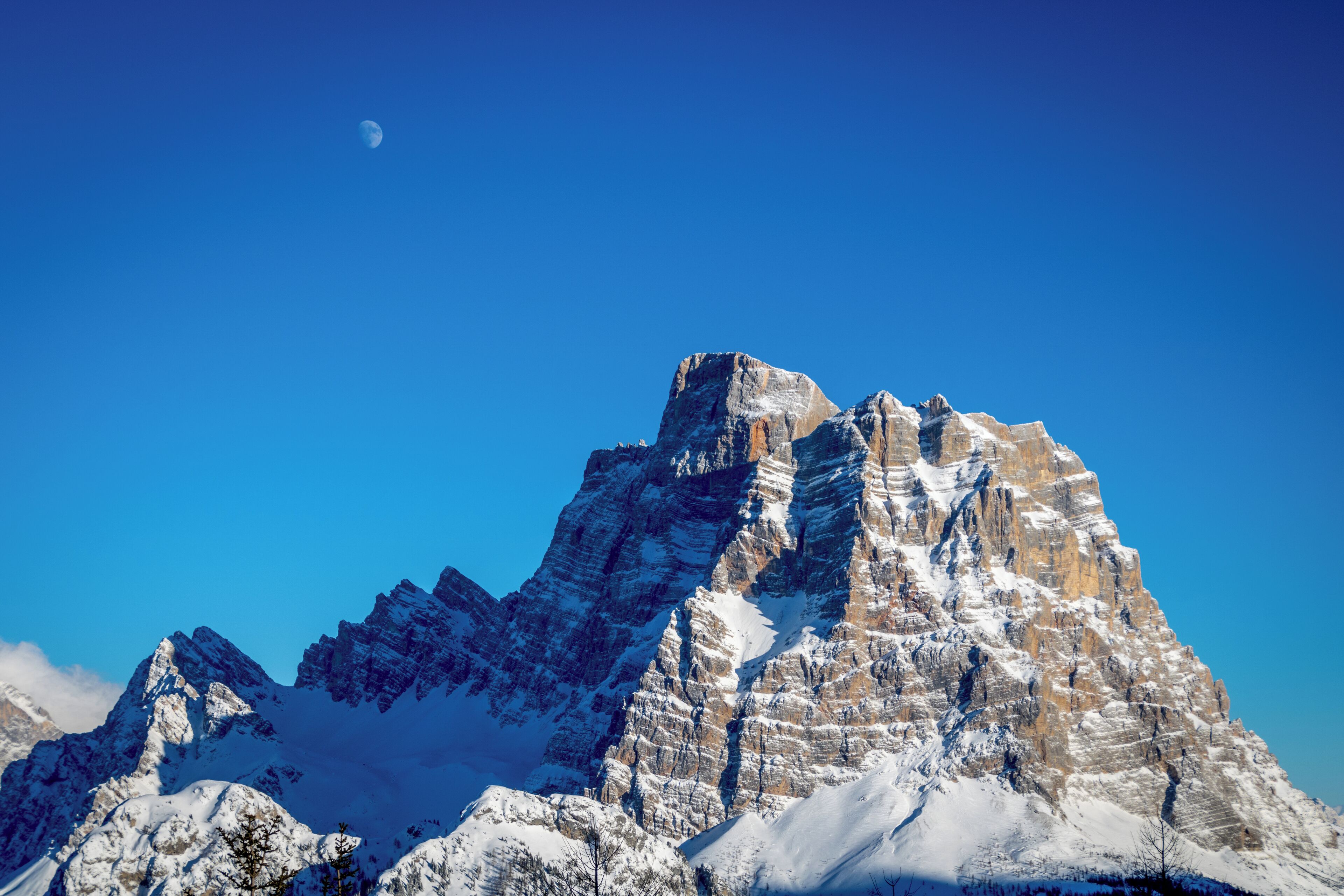 A snow-covered mountain peak with a clear blue sky and a crescent moon.
