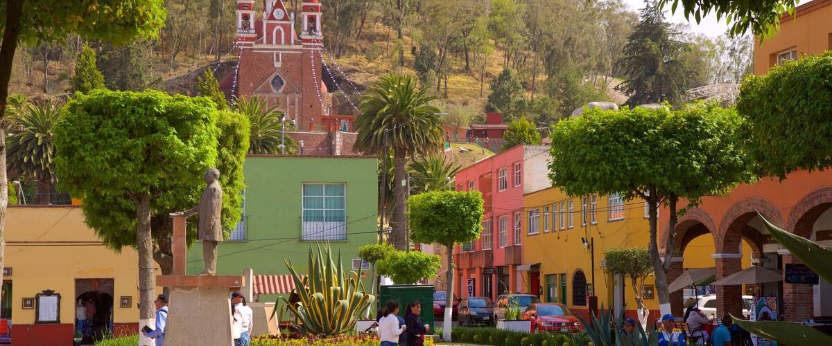 A plaza with a statue, colorful buildings, and a hill with a church in the background.