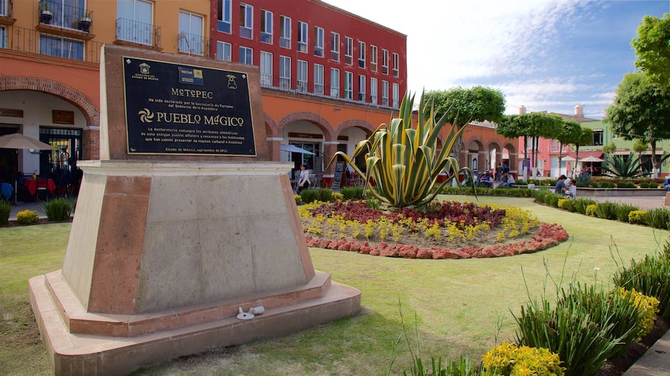 A monument with a plaque in a public square surrounded by a garden with various plants and flowers.