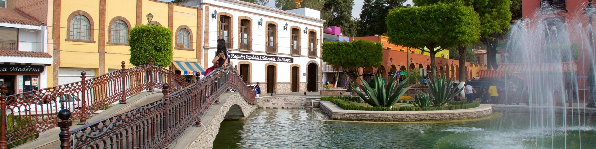 Un puente sobre un estanque con una fuente, rodeado de edificios y árboles.