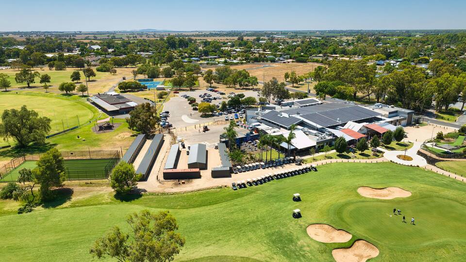 An aerial view of a golf course with multiple bunkers, a parking lot, and surrounding buildings.