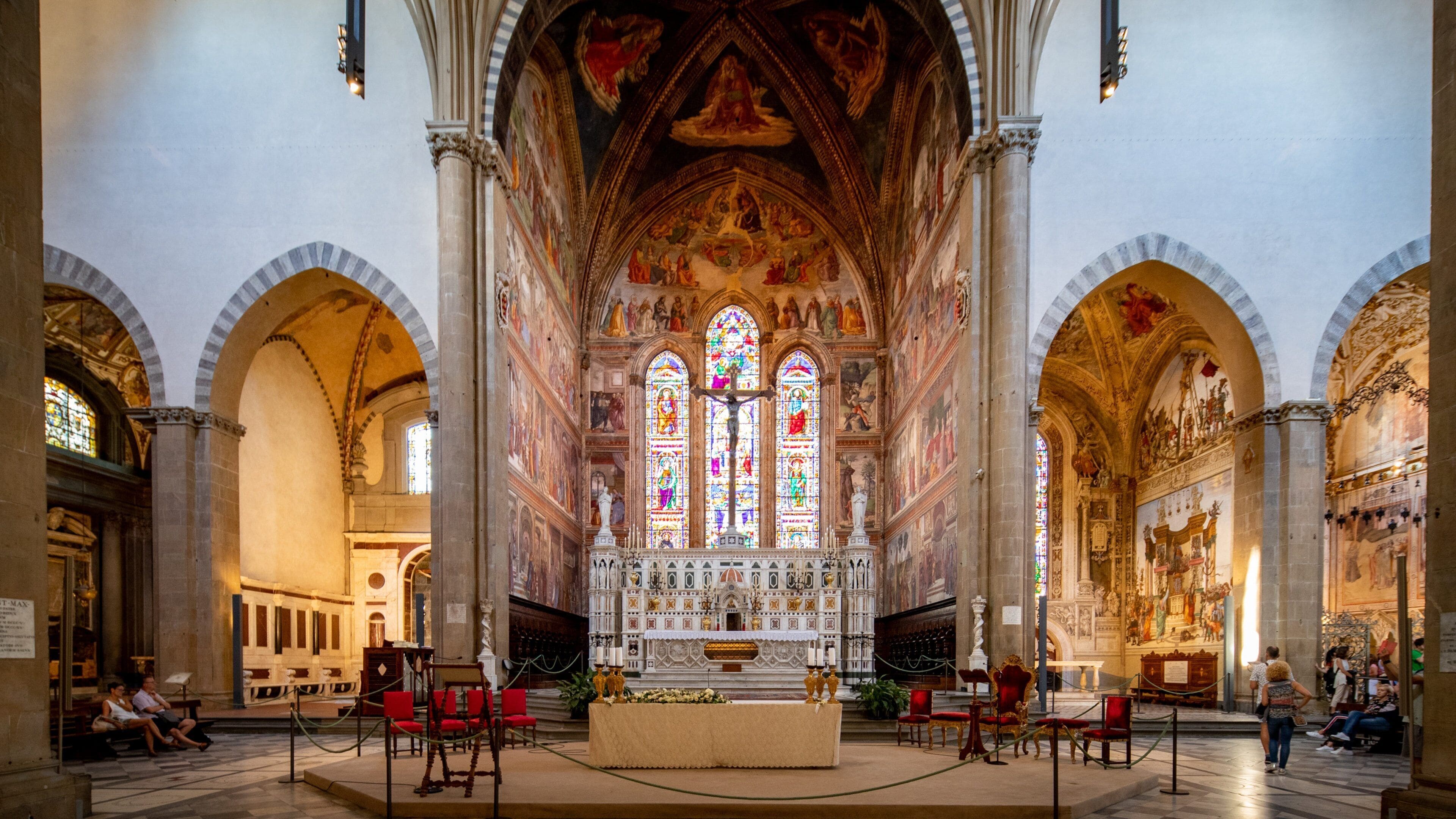 Interior de una catedral con altar central, vidrieras y frescos detallados.
