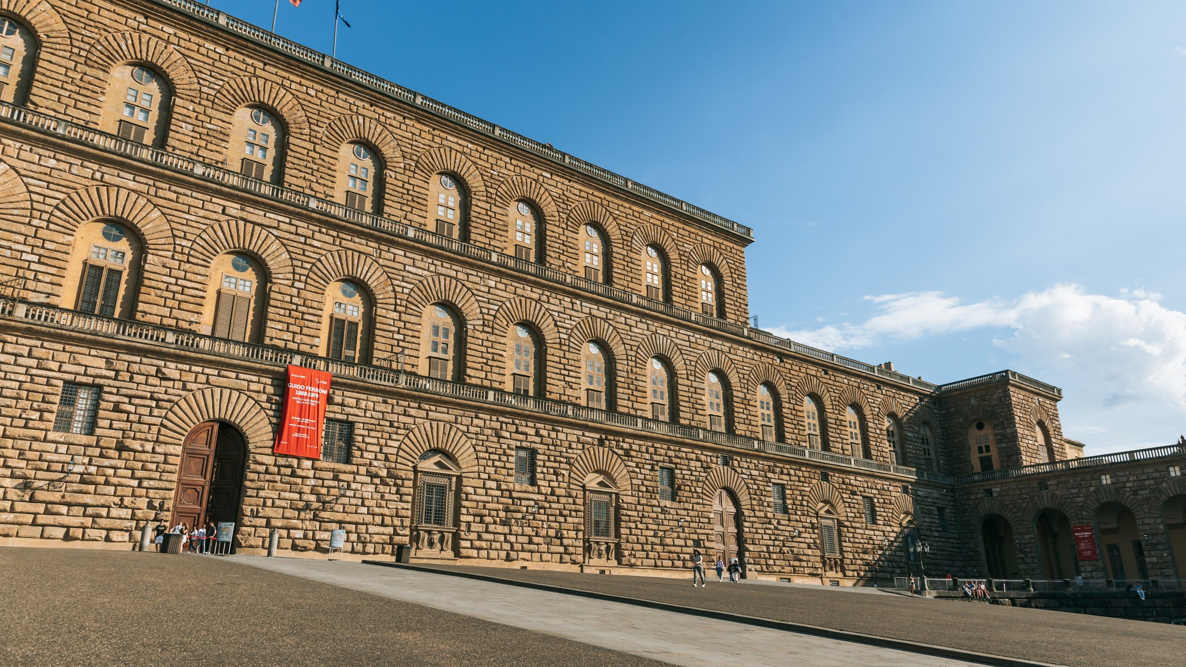 Un grand bâtiment en pierre, doté de fenêtres en arc de cercle et orné d’une bannière rouge.