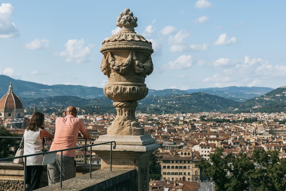 A stone balustrade with a decorative urn, overlooking a cityscape with a dome and hills in the background.