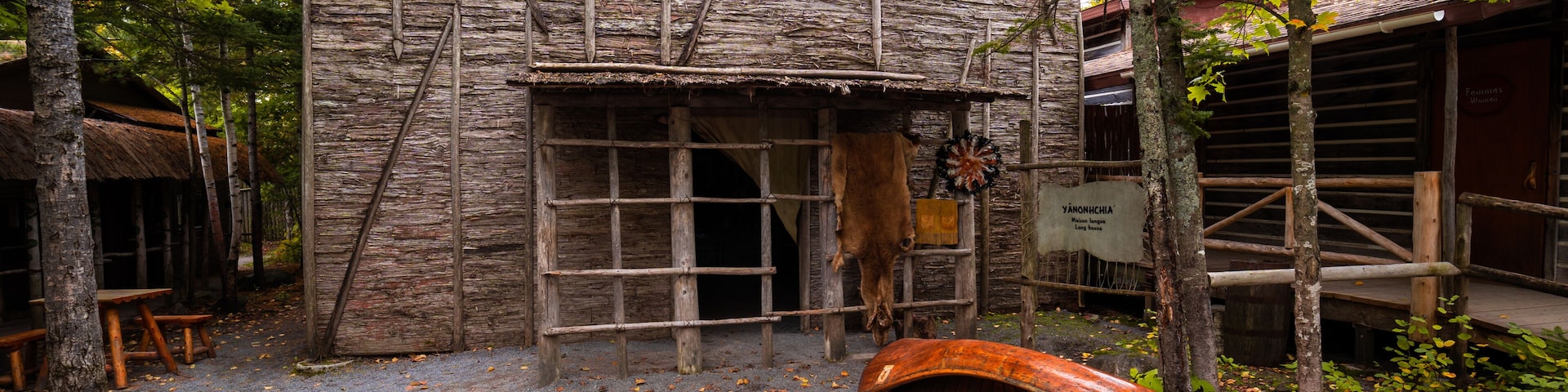 A rustic wooden building with a thatched roof, surrounded by trees and a fallen log.