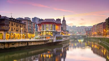 A river with buildings reflecting in the water, a bridge, and a tower in the background.