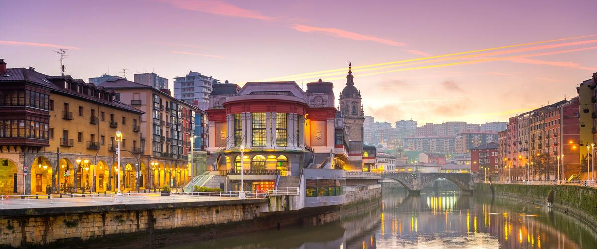 A river with buildings reflecting in the water, a bridge, and a tower in the background.