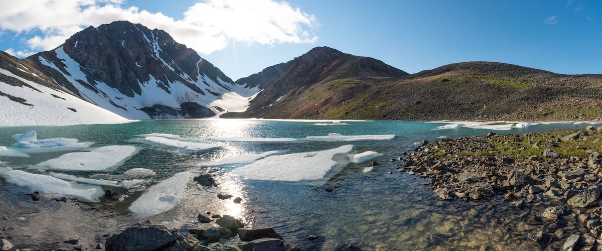 A glacier lake surrounded by mountains with snow patches and icebergs.