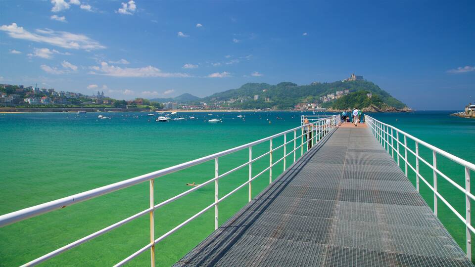 A pier extending into turquoise waters with a mountainous backdrop and a clear sky.