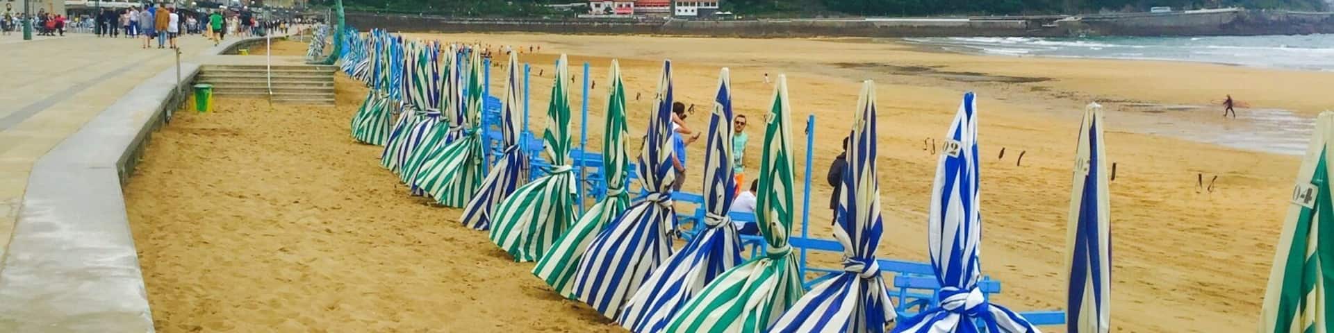 A beach with striped umbrellas lined up along the shore, a sandy beach, and buildings in the background.