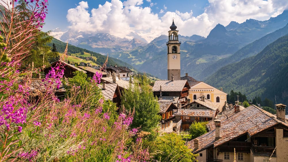 Ein Dorf mit traditioneller Architektur, einem Kirchturm und Bergen im Hintergrund.