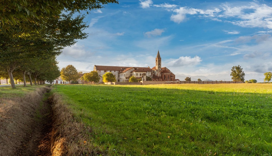 Staffarda di Revello, Saluzzo, Italy - October 8, 2021: Abbey of Santa Maria di Staffarda of Roman Gothic style (XII century) between green meadows and blue sky