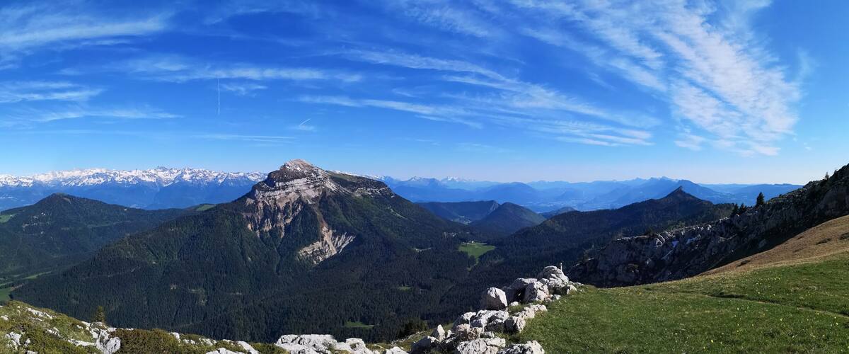 A mountain landscape with a prominent peak, a clear blue sky, and a hiker's foot on a wooden railing.